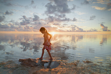 Girl wading in ocean surf on tranquil sunset beach - HOXF01402