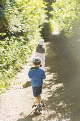 Junge und Mädchen gehen auf einem sonnigen, von Bäumen gesäumten Parkweg - HOXF01423