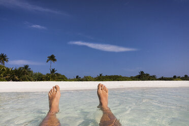 Personal perspective barefoot man floating in tropical ocean surf with view of beach - HOXF01424