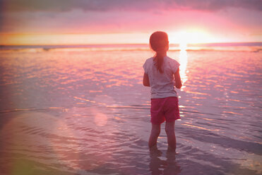 Pensive girl wading in ocean on tranquil sunset beach - HOXF01426