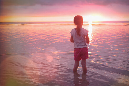 Nachdenkliches Mädchen watet im Meer am ruhigen Strand bei Sonnenuntergang - HOXF01426