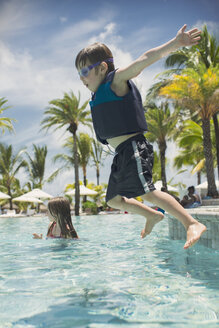 Boy jumping into sunny tropical swimming pool - HOXF01431