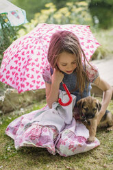 Mädchen mit Hundewelpe hält herzförmigen Regenschirm im Gras - HOXF01434