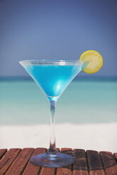Blauer Cocktail mit Zitronenscheibe im Martiniglas am sonnigen tropischen Strand - HOXF01444