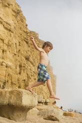 Junge in Badehose springt auf Strandfelsen - HOXF01447