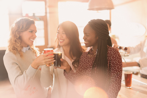 Freundinnen stoßen mit Biergläsern an der Bar an, lizenzfreies Stockfoto