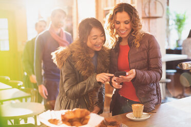 Freundinnen benutzen Mobiltelefon in einem Café - HOXF01466