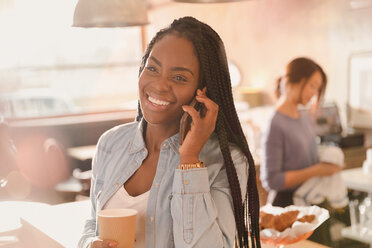 Lächelnde Frau, die in einem Café mit ihrem Handy telefoniert und Kaffee trinkt - HOXF01473