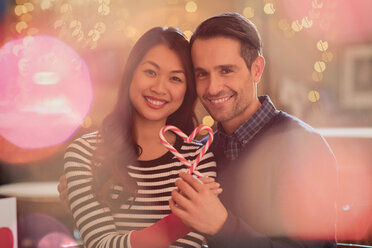 Portrait smiling couple holding heart-shape candy canes - HOXF01475