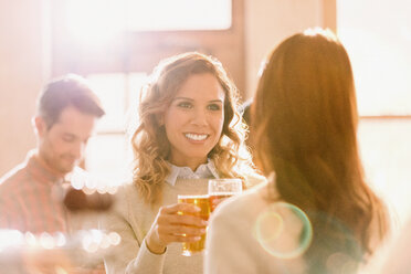 Smiling women friends toasting beer glasses in sunny bar - HOXF01482