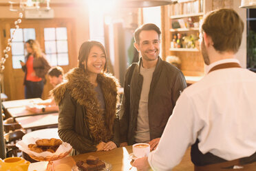 Barista serving coffee to couple at counter in cafe - HOXF01484