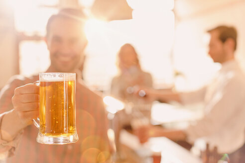Porträt eines lächelnden Mannes mit Bierkrug in einer hell erleuchteten Bar - HOXF01488