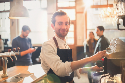 Porträt lächelnder männlicher Barista mit Espressomaschine in einem Café, lizenzfreies Stockfoto