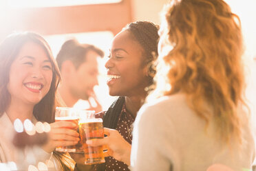 Lächelnde Freundinnen stoßen mit Biergläsern in einer Bar an - HOXF01498