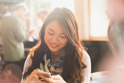 Lächelnde chinesische Frau, die in einem Café eine SMS mit ihrem Handy schreibt, lizenzfreies Stockfoto