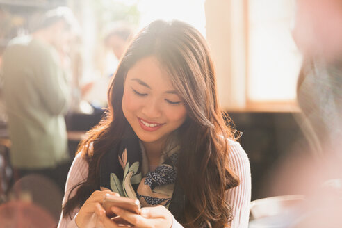 Lächelnde chinesische Frau, die in einem Café eine SMS mit ihrem Handy schreibt - HOXF01504