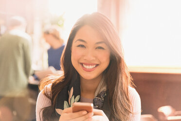 Porträt einer lächelnden chinesischen Frau, die in einem Café eine SMS mit ihrem Handy schreibt - HOXF01515