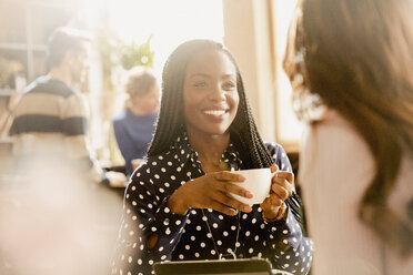 Lächelnde Freundinnen trinken Kaffee und unterhalten sich in einem Cafe - HOXF01520