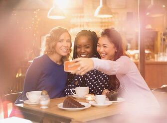 Smiling women friends taking selfie with camera phone at cafe table - HOXF01521