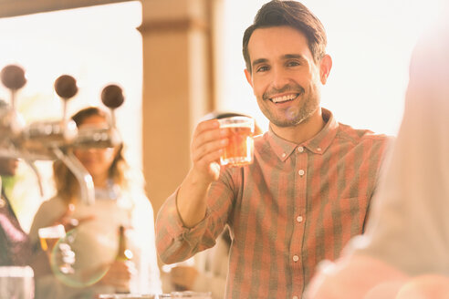 Porträt eines lächelnden Mannes, der an einer Bar mit einem Bierglas anstößt - HOXF01523