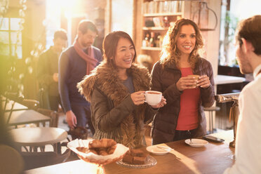 Women talking to barista at cafe counter - HOXF01528