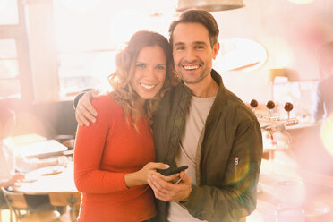 Porträt liebevolles lächelndes Paar, das in einer Bar ein Mobiltelefon benutzt - HOXF01541