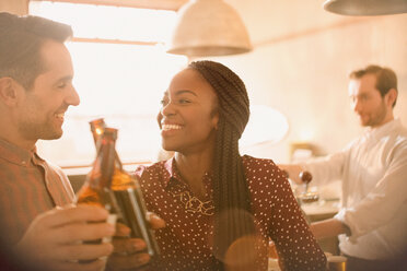 Lächelndes Paar, das in einer Bar mit Bierflaschen anstößt - HOXF01543