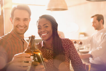 Porträt lächelndes Paar, das in einer Bar auf Bierflaschen anstößt - HOXF01556