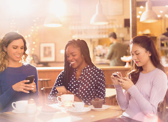 Freundinnen, die mit ihren Handys am Kaffeetisch SMS schreiben - HOXF01559