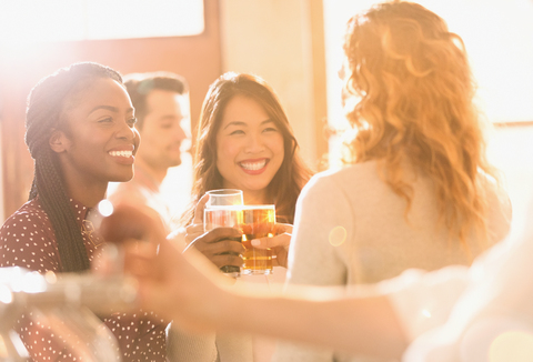 Lächelnde Freundinnen stoßen mit Biergläsern in einer sonnigen Bar an, lizenzfreies Stockfoto