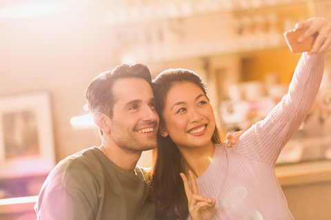 Lächelndes Paar gestikuliert Friedenszeichen nehmen Selfie mit Kamera-Handy, lizenzfreies Stockfoto