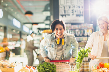 Porträt verspielte junge Frau mit Einkaufswagen Lebensmittelgeschäft Einkaufen im Markt - HOXF01571