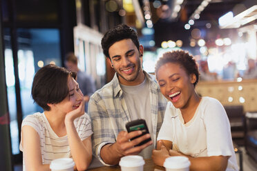 Junge Freunde benutzen ihr Handy, schreiben SMS und lachen im Café - HOXF01581