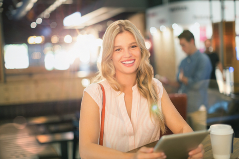 Porträt einer lächelnden jungen Frau, die in einem Café ein digitales Tablet benutzt, lizenzfreies Stockfoto