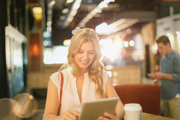Lächelnde junge Frau, die ein digitales Tablet benutzt und Kaffee in einem Café trinkt - HOXF01593