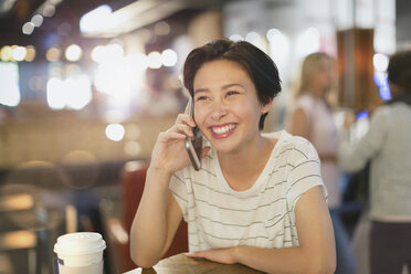 Lächelnde junge Frau, die in einem Café mit ihrem Handy telefoniert - HOXF01598