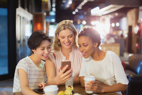 Junge Frauen, die ein Handy benutzen und Kaffee in einem Café trinken, lizenzfreies Stockfoto