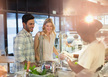 Female worker helping young couple at deli counter in grocery store market - HOXF01637