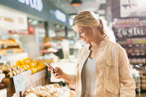 Junge Frau benutzt Mobiltelefon in einem Lebensmittelgeschäft, lizenzfreies Stockfoto