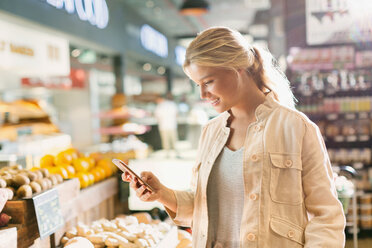 Young woman using cell phone in grocery store market - HOXF01640