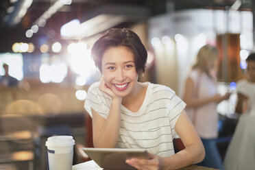 Porträt einer lächelnden jungen Frau, die ein digitales Tablet benutzt und in einem Café Kaffee trinkt - HOXF01646