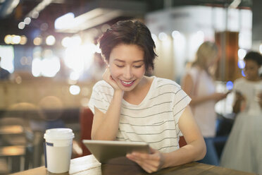 Junge Frau, die ein digitales Tablet benutzt und in einem Café Kaffee trinkt - HOXF01648