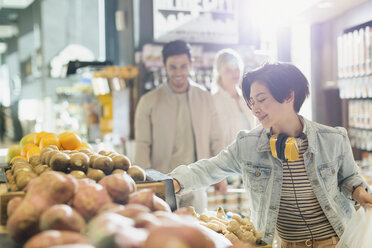 Junge Frau mit Kopfhörern beim Lebensmitteleinkauf und beim Durchstöbern von Produkten auf dem Markt - HOXF01649