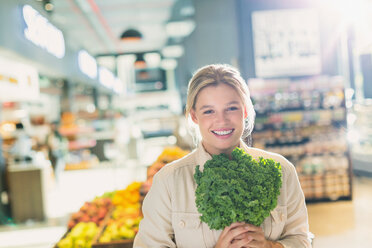 Portrait smiling young woman holding bunch of kale in grocery store market - HOXF01666