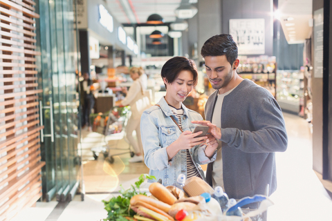 Junges Paar benutzt Mobiltelefon in einem Lebensmittelgeschäft, lizenzfreies Stockfoto