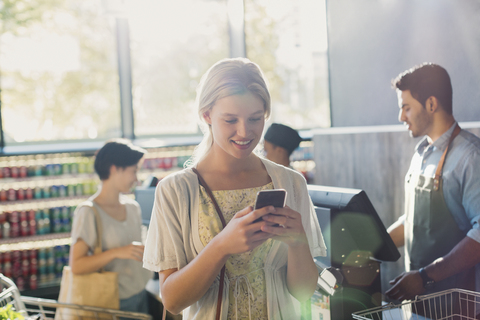 Junge Frau benutzt Mobiltelefon in einem Lebensmittelgeschäft, lizenzfreies Stockfoto