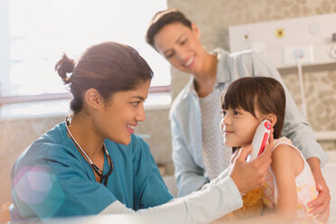 Female nurse using digital thermometer in ear of girl patient in examination room - HOXF01690