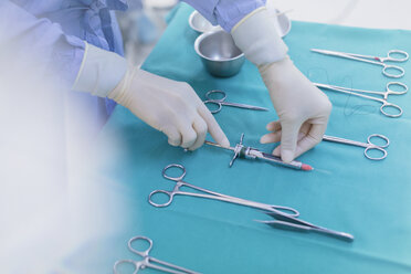 Chirurg mit Gummihandschuhen bereitet chirurgische Instrumente auf einem Tablett vor - HOXF01691