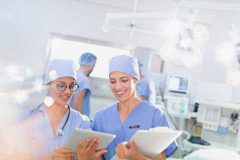 Lächelnde Chirurginnen mit digitalem Tablet und Klemmbrett im Operationssaal, lizenzfreies Stockfoto