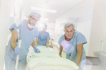 Entschlossene Chirurgen schieben eine Bahre den Krankenhausflur entlang - HOXF01705